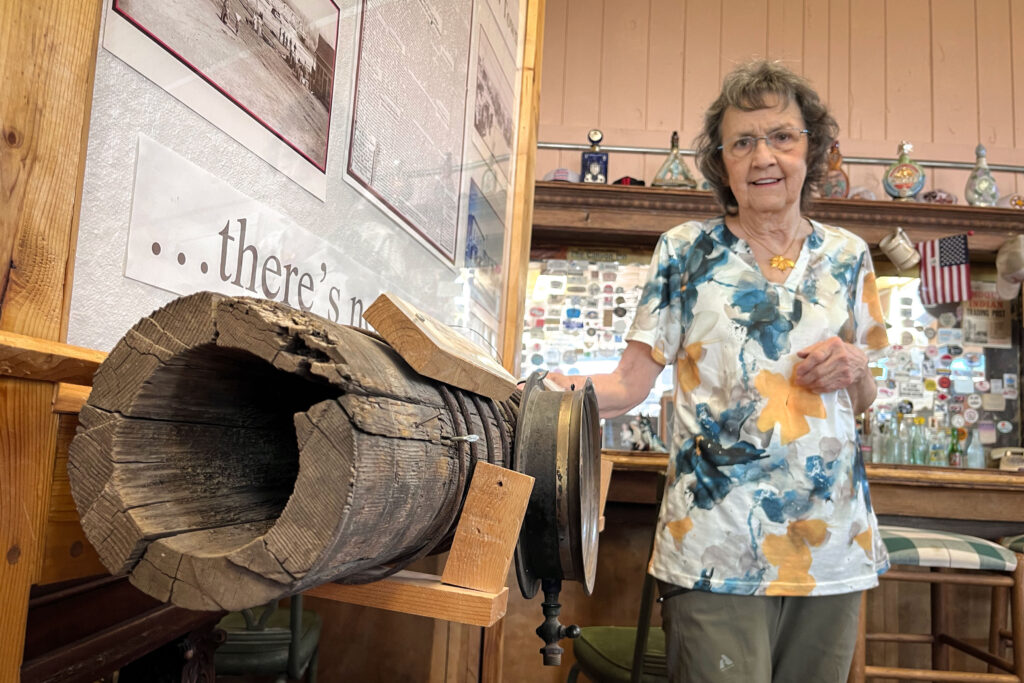 Myton Mayor Kathleen Cooper stands next to an old water pipeline in the town’s historical museum, Oct. 1, 2025. She says many of the town’s current pipes leak badly, but Myton doesn’t have the money to replace them.